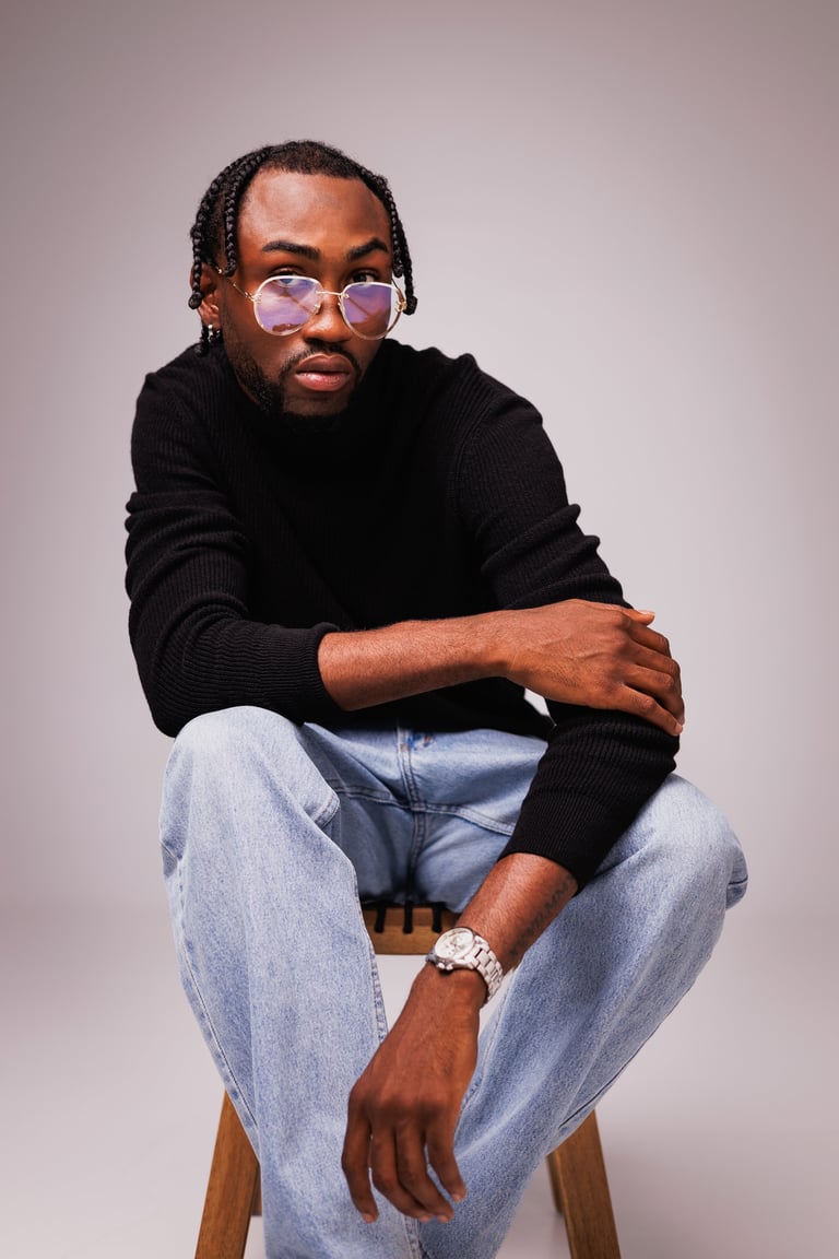 Stylish african american man in eyeglasses and black turtleneck looking at camera on chair on grey background